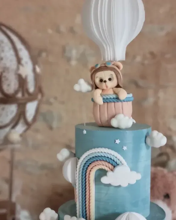 Ourson comestible modelé à la main dans une montgolfière sur un gâteau de baptême bleu ciel