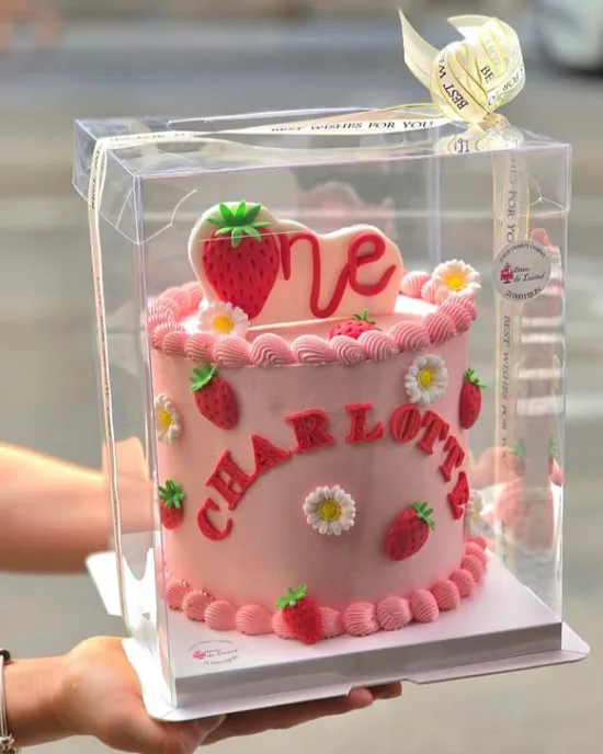 Gâteau cake design rose sur présentoir avec topper one, fraises rouges, marguerites blanches et prénom Charlotte en lettres rouges